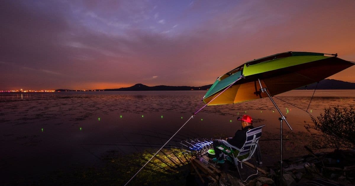 Man Fishing At Night Under Umbrella.